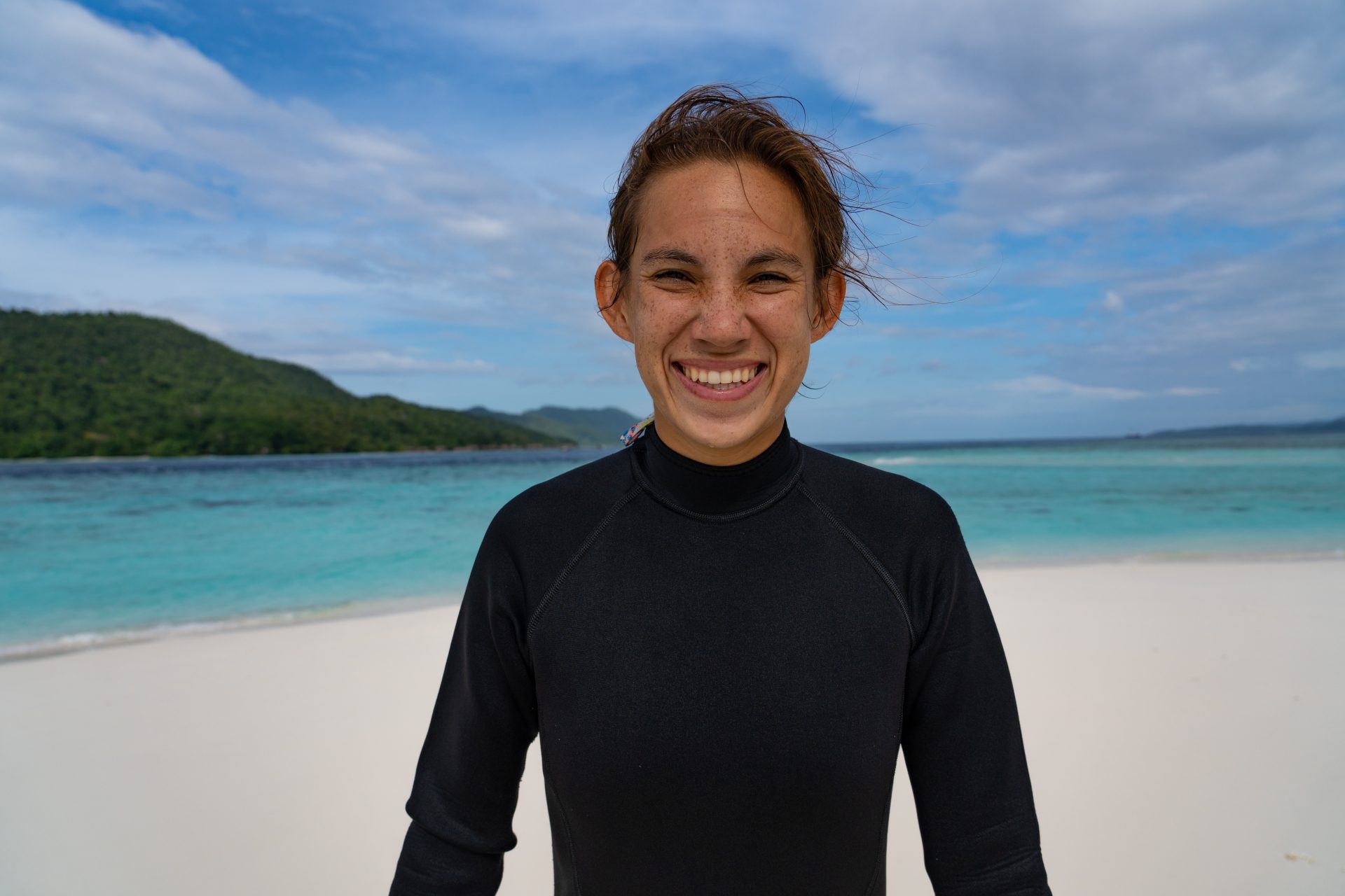 Wini smiling on a sandbar with a scuba wetsuit on, in Raja Ampat, Indonesia.