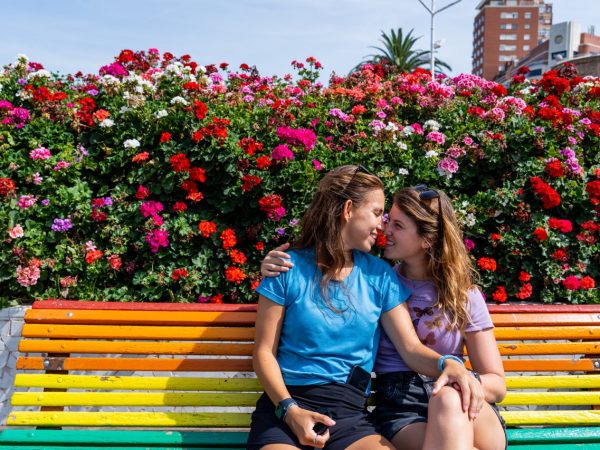 Valencia rainbow bench with colorful flowers behind and two lesbians.