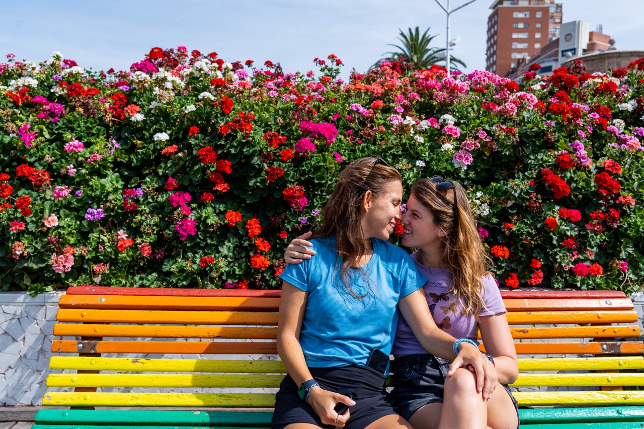 Valencia rainbow bench with colorful flowers behind and two lesbians.