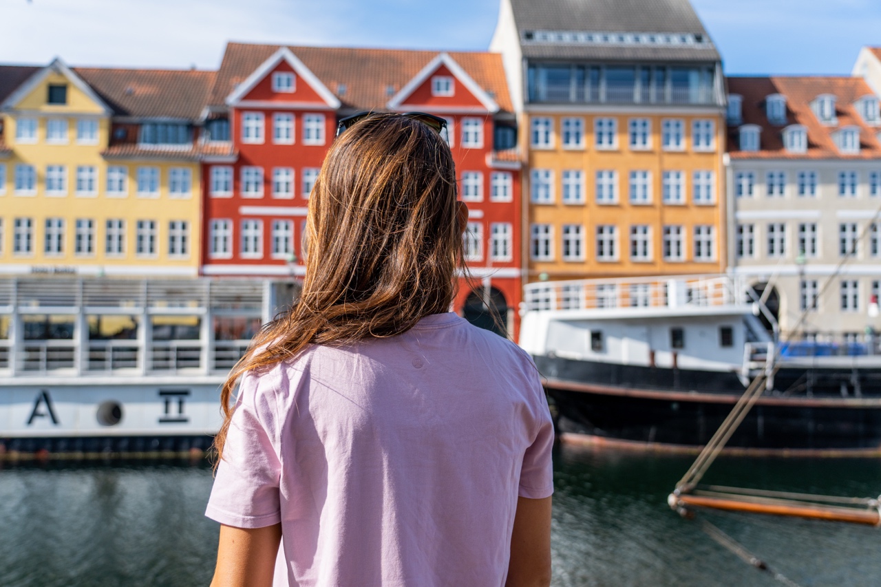 Woman in pink shirt standing in front of Nyhavn, Copenhagen, Denmark canal and colorful buildings.